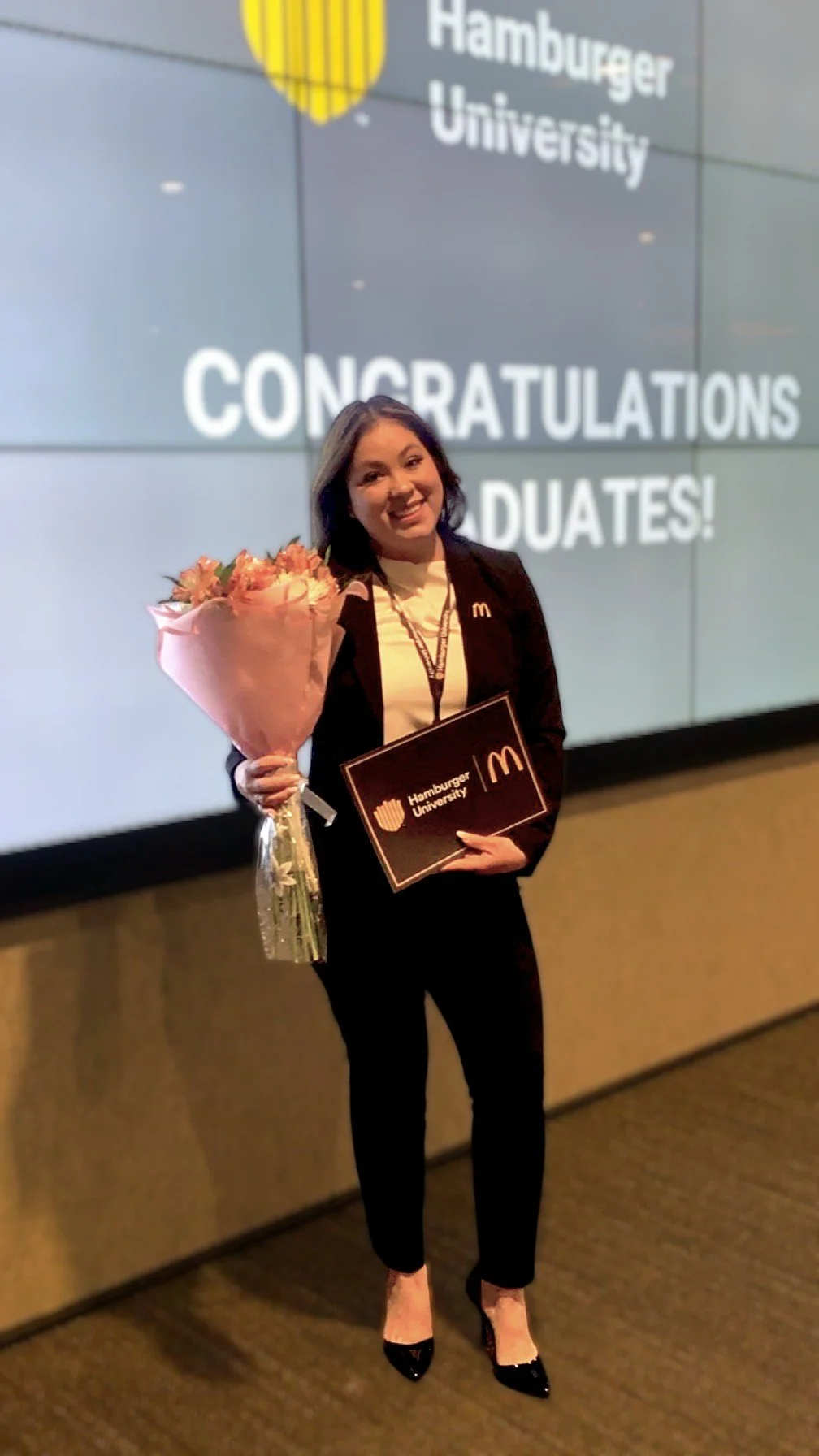A JJC leader holding her Hamburger University diploma and flowers at graduation